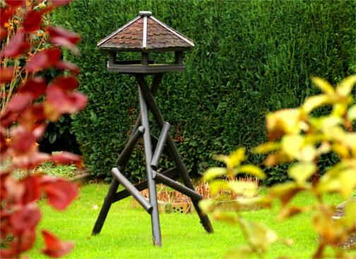 Ein Dreibein-Vogelhaus steht in einem Garten, es sind keine Vögel zu sehen